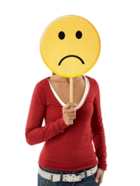 A woman holding a round yellow frowning face in front of her face.